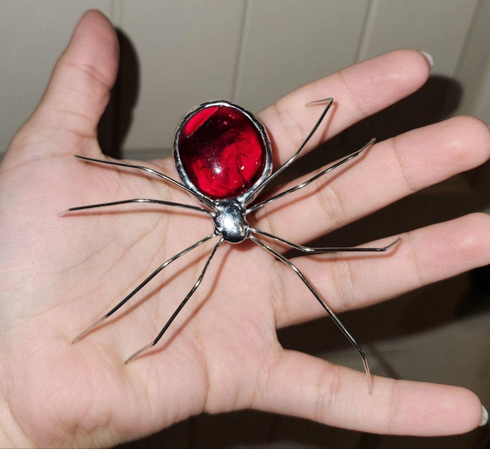 3D stained glass pebble spider being held in hand. The pebble is bright red.