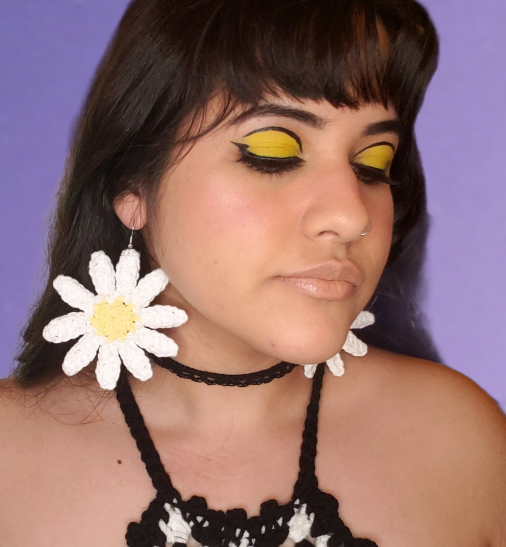 Large crocheted daisy earrings displayed on model. White long petals with yellow center.