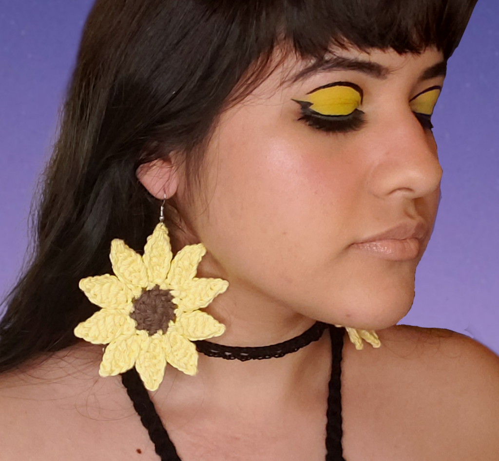 Large crocheted yellow sunflower earrings with brown centers displayed on model.